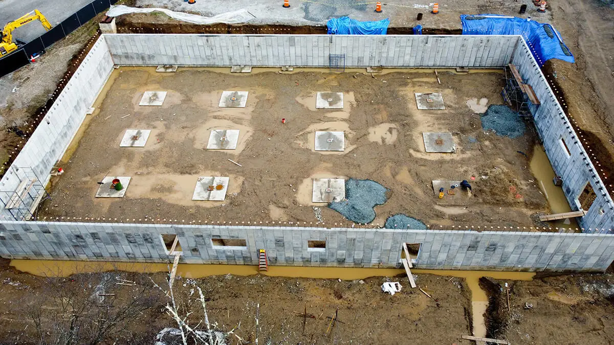 An aerial view of a construction site showcasing a completed concrete foundation wall with footing pads, highlighting structural groundwork in progress