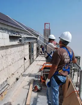 Crew members equipped with harnesses and safety gear perform facade repairs on a suspended platform—emphasizing high-rise job site safety