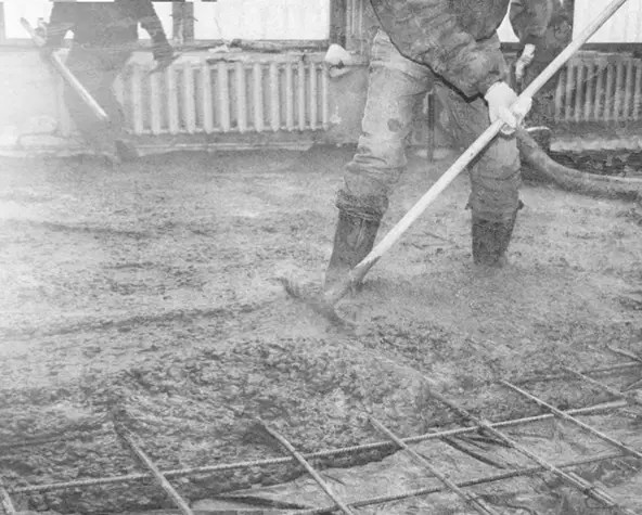 Construction workers leveling freshly poured concrete over rebar for a parking garage floor during structural installation