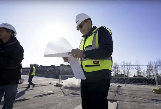 T.G. Basile Construction supervisor inspects project blueprints on-site, ensuring detailed planning and execution in a safe, well-managed environment