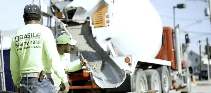 T.G. Basile workers guide concrete from a cement truck chute during a construction project, showcasing hands-on expertise and site readiness