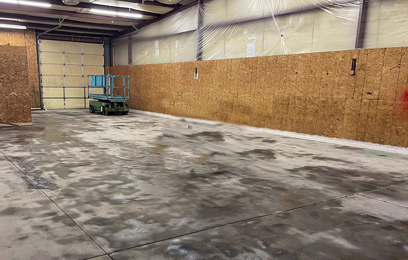 A warehouse concrete floor shows visible surface texture and discoloration after an acid etching treatment for coating preparation
