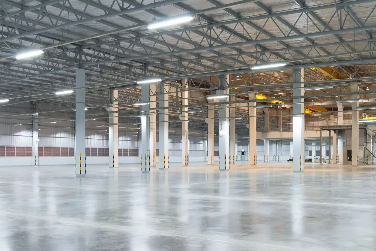 A large, clean warehouse featuring a smooth, polished concrete floor with bright overhead lighting and high ceilings with exposed beams