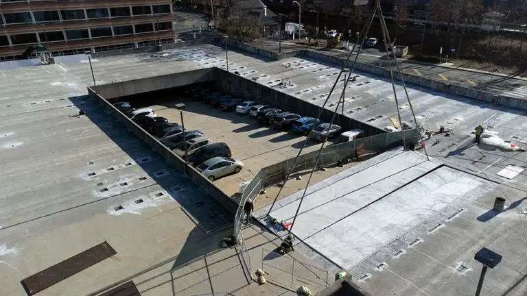 A large crane lifts a concrete slab during parking garage restoration, highlighting structural repair and proactive maintenance work
