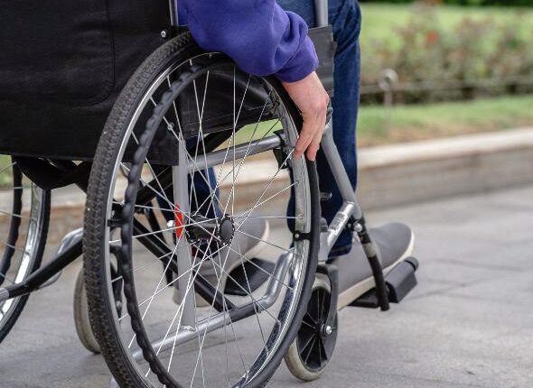 Close-up of a person in a wheelchair using a smooth ADA-accessible sidewalk with proper slope and curb design