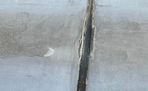 Cracked and worn expansion joint in a concrete slab. The surface shows signs of deterioration, with exposed material and discoloration
