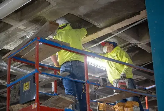 Workers in safety gear restoring a concrete ceiling on lift scaffolding during a parking garage structural maintenance project