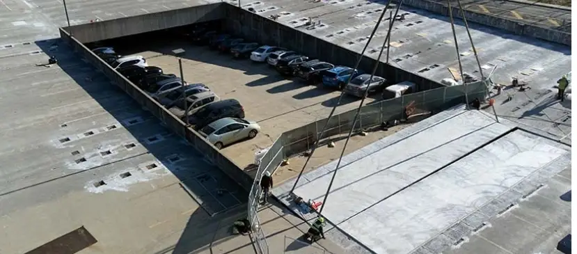 Structural maintenance of a parking garage with cranes and safety fencing protecting vehicles during restoration work