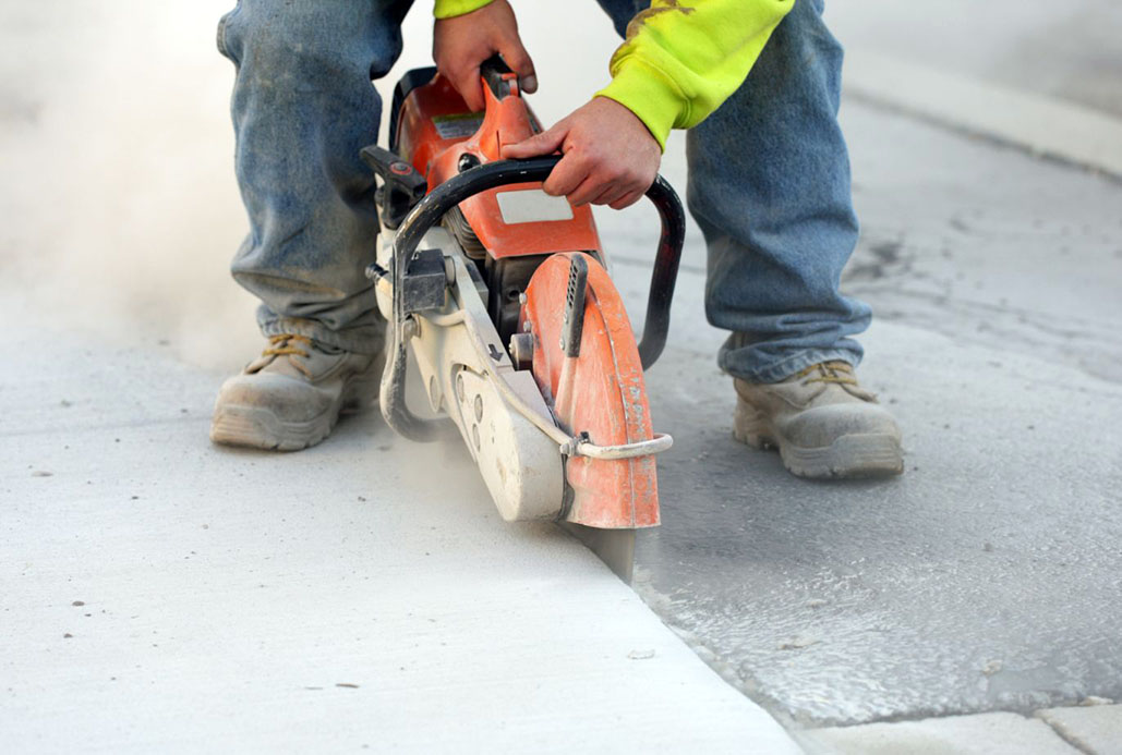 A construction worker uses a handheld concrete saw to make precise cuts in a sidewalk during pavement repair or installation