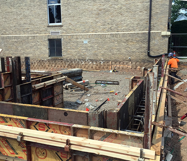 Crews prepare formwork and rebar placement for a structural concrete pour along the base of an existing building