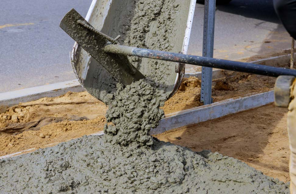 Concrete being poured from a truck chute and spread using a rake to form a road slab base, highlighting the fresh mix and work-in-progress surface
