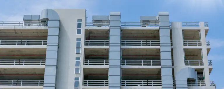 A modern multilevel parking structure under clear blue skies, showcasing its concrete framework, ventilation systems, and open-air design