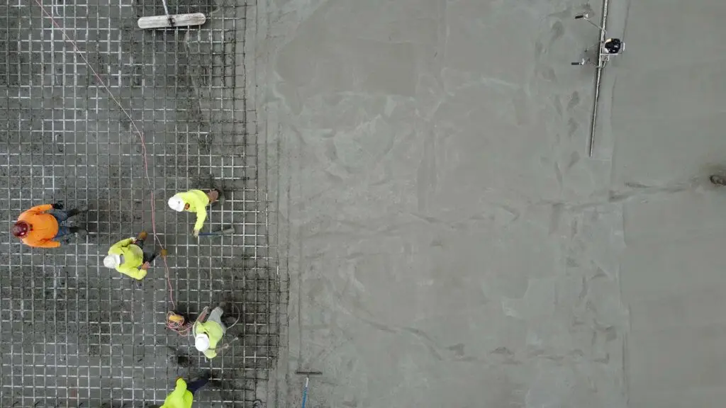 Top-down view of construction crew pouring and finishing concrete over rebar grid for a high-strength slab foundation