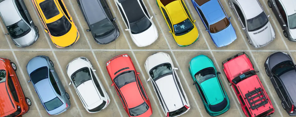 Top-down view of various brightly colored vehicles neatly parked in marked spaces on a concrete parking deck, illustrating urban vehicle density