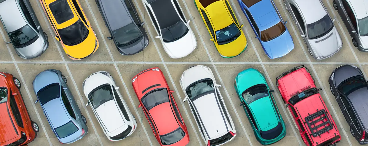 Top-down view of various brightly colored vehicles neatly parked in marked spaces on a concrete parking deck, illustrating urban vehicle density