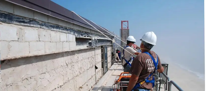 T.G. Basile team members secured with safety harnesses while working on a high-rise restoration project overlooking the beach, ensuring OSHA compliance