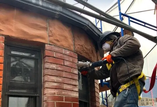 Construction worker wearing full PPE while restoring a brick building’s facade, highlighting T.G. Basile’s commitment to job site safety and precision