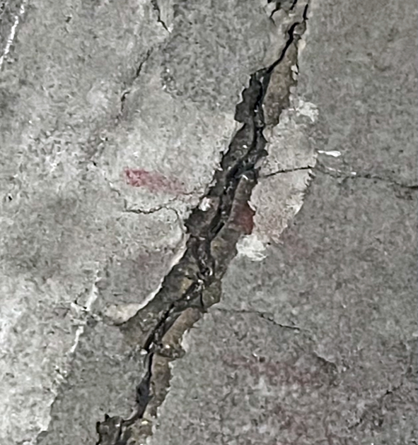 Close-up of a deep crack in a concrete surface showing signs of spalling and delamination, often caused by moisture infiltration and structural stress