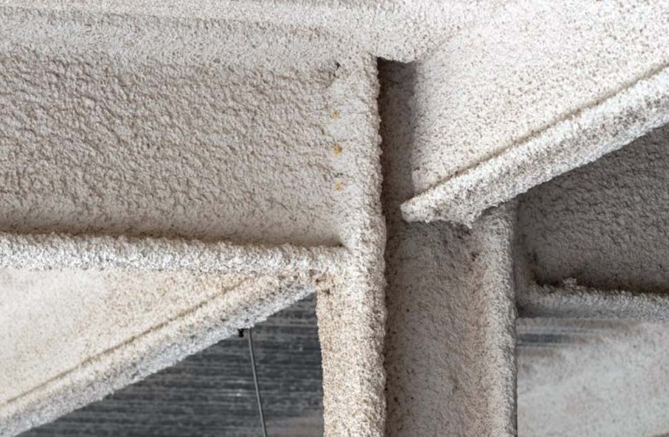 Close-up of structural steel beams coated with spray-applied fire-resistive material (SFRM), enhancing fire protection in commercial buildings