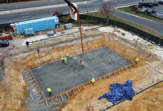 Aerial view of workers pouring structural concrete foundation at a commercial construction site, ensuring strength and long-term stability