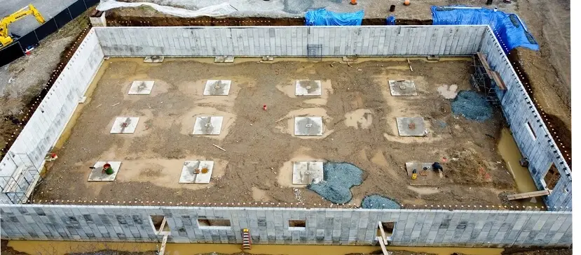 Aerial view of a construction site showing completed concrete walls and foundation footings for a new commercial or industrial structure