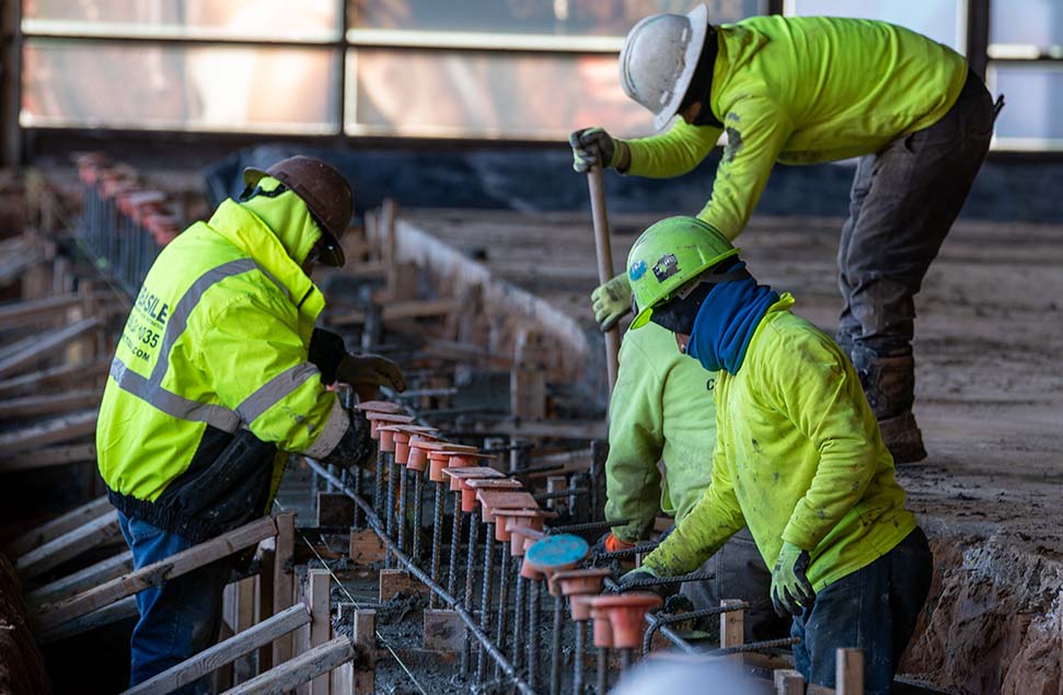 Construction workers installing rebar and safety caps in a concrete form to reinforce a structural slab, ensuring durability and worker safety
