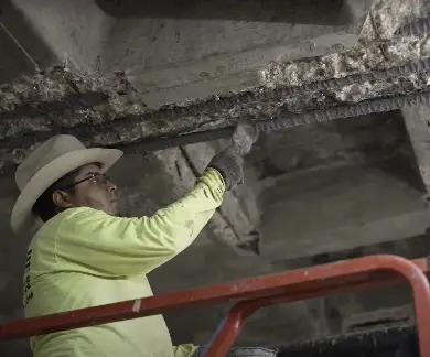 Construction professional repairs deteriorated concrete and exposed rebar on ceiling, enhancing structure's durability and safety