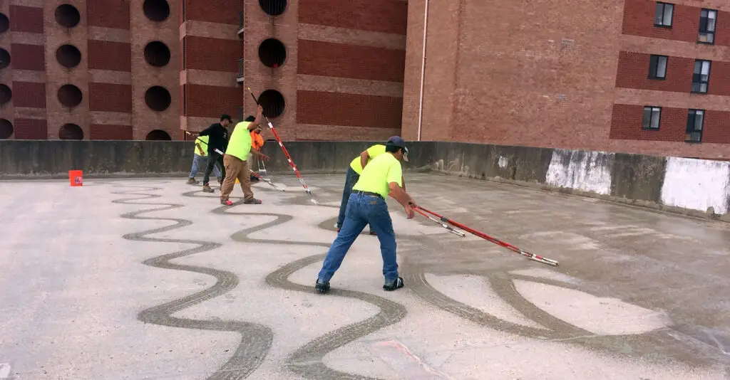 Crew members apply waterproofing sealant to the exposed top level of a parking garage, protecting the concrete from moisture and structural damage