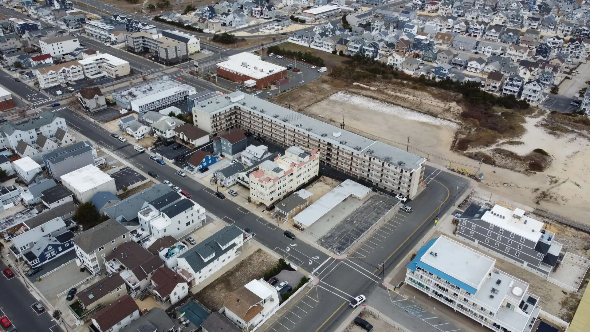 Drone view of a coastal residential area in Seaside Heights, NJ, showing facade repair work on a large beachfront apartment complex near the dunes