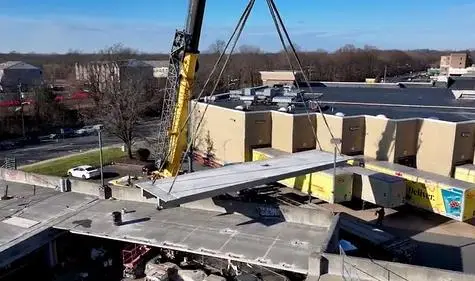 A crane lifts a large concrete panel during structural repairs to the Somerville, NJ parking garage under clear blue skies