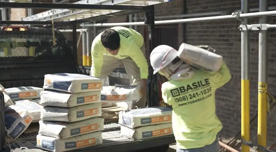 Construction crew unloading and carrying mortar mix bags from a truck for a historic building facade repair in Yonkers, New York