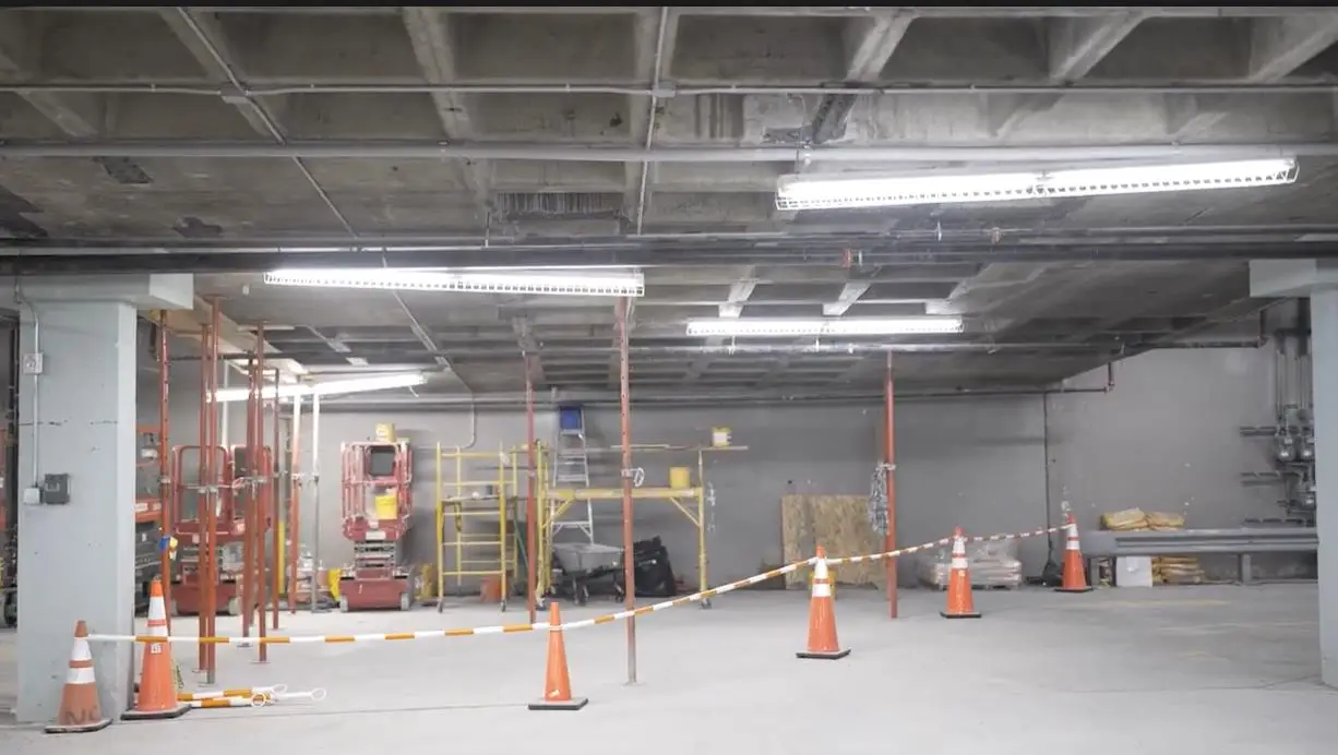 Interior of a Newark parking garage under repair, featuring scaffolding, support jacks, and safety cones during waterproofing work