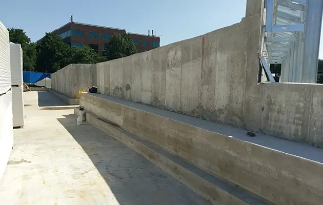 Newly poured concrete foundation walls and tiered steps set against structural framing at a commercial construction site