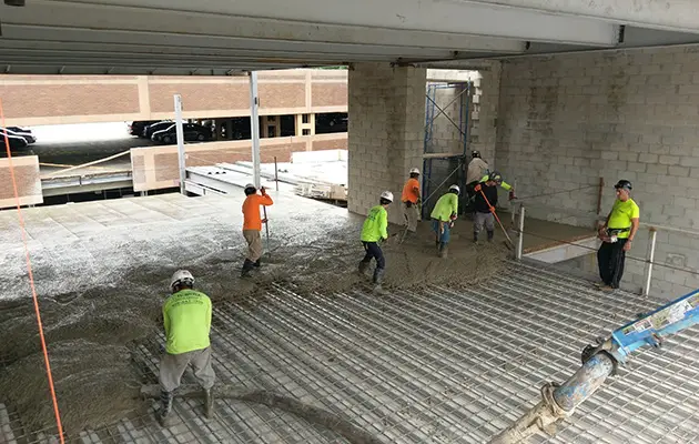 Construction crew placing and leveling concrete over a rebar-reinforced metal deck inside a partially enclosed commercial space