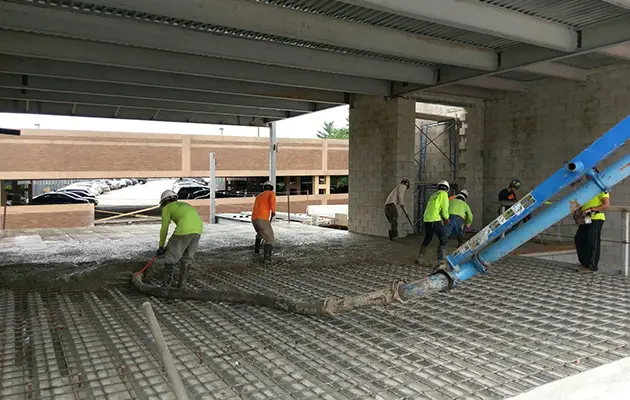 Crew pouring concrete slab over a metal deck with rebar reinforcement inside a partially enclosed commercial structure