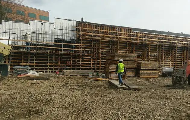 Workers assembling extensive wood and steel formwork for vertical concrete wall placement at a commercial construction location