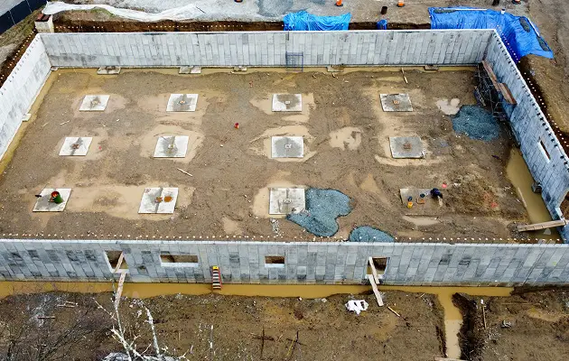 Aerial view of a construction site showing concrete footings, foundation walls, and prep work for slab and drainage