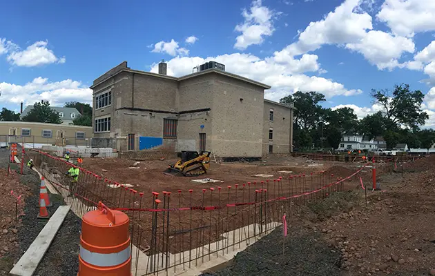 Excavation and rebar installation in progress at a construction site adjacent to an existing building under a bright sky