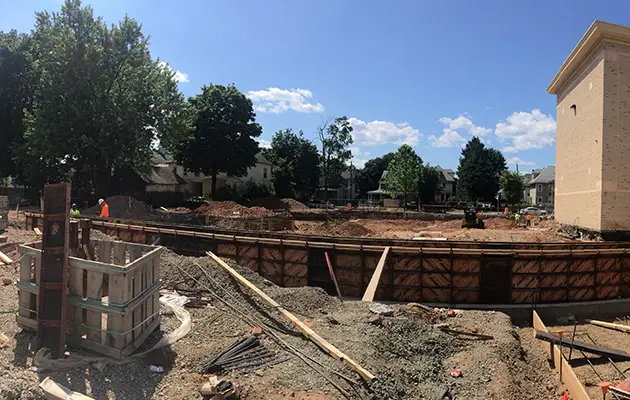 Construction site showing wooden formwork for concrete foundation walls and early-stage utility and drainage preparations