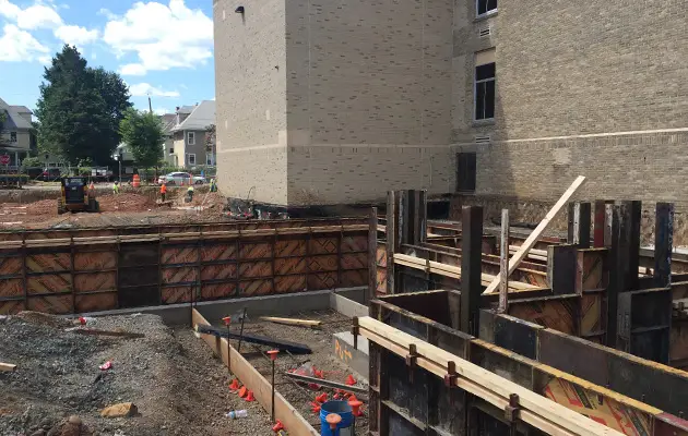 Workers assemble wood and steel formwork around footings and rebar as part of the foundation wall construction process