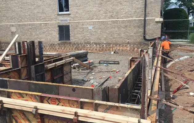 Crews prepare formwork and rebar placement for a structural concrete pour along the base of an existing building