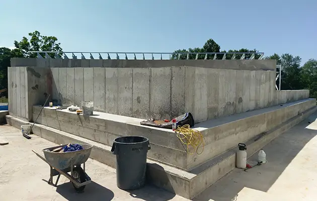 Solid concrete walls and tiered base platform shown post-pour with construction tools on-site under clear daylight conditions