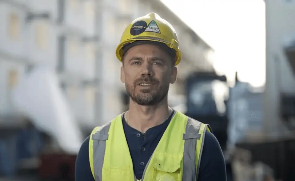 A project executive in a hard hat and high-vis vest stands confidently on-site, ensuring safety and progress on construction work