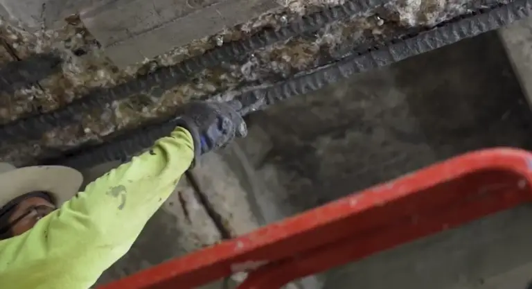 Worker repairing exposed rebar in a concrete ceiling during parking garage structural restoration and maintenance.