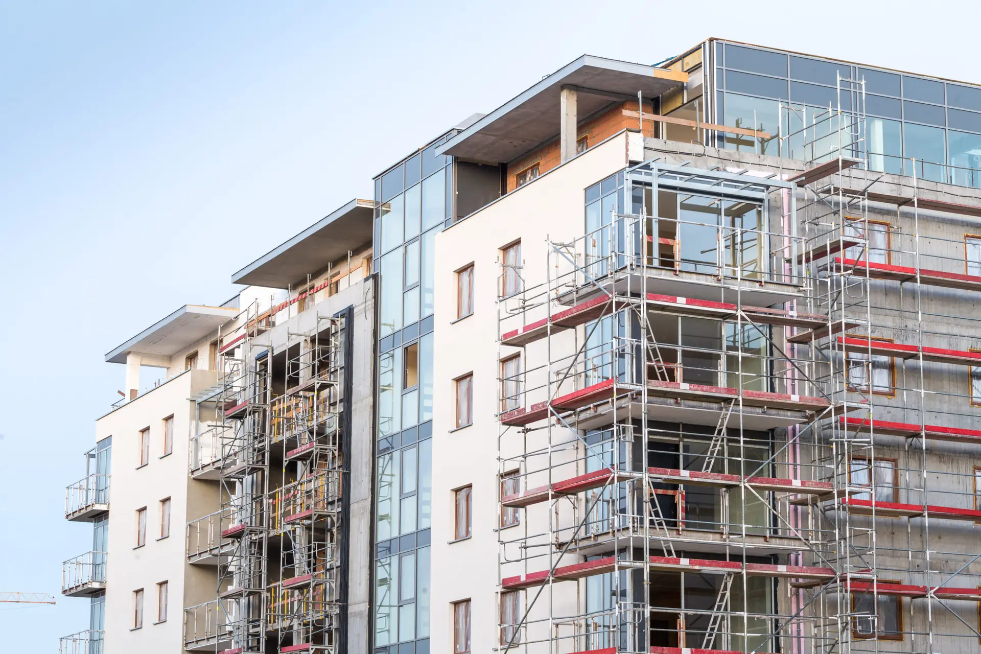 View of a multi-story apartment building under construction with scaffolding in place. Features glass panels, balconies, and unfinished exteriors