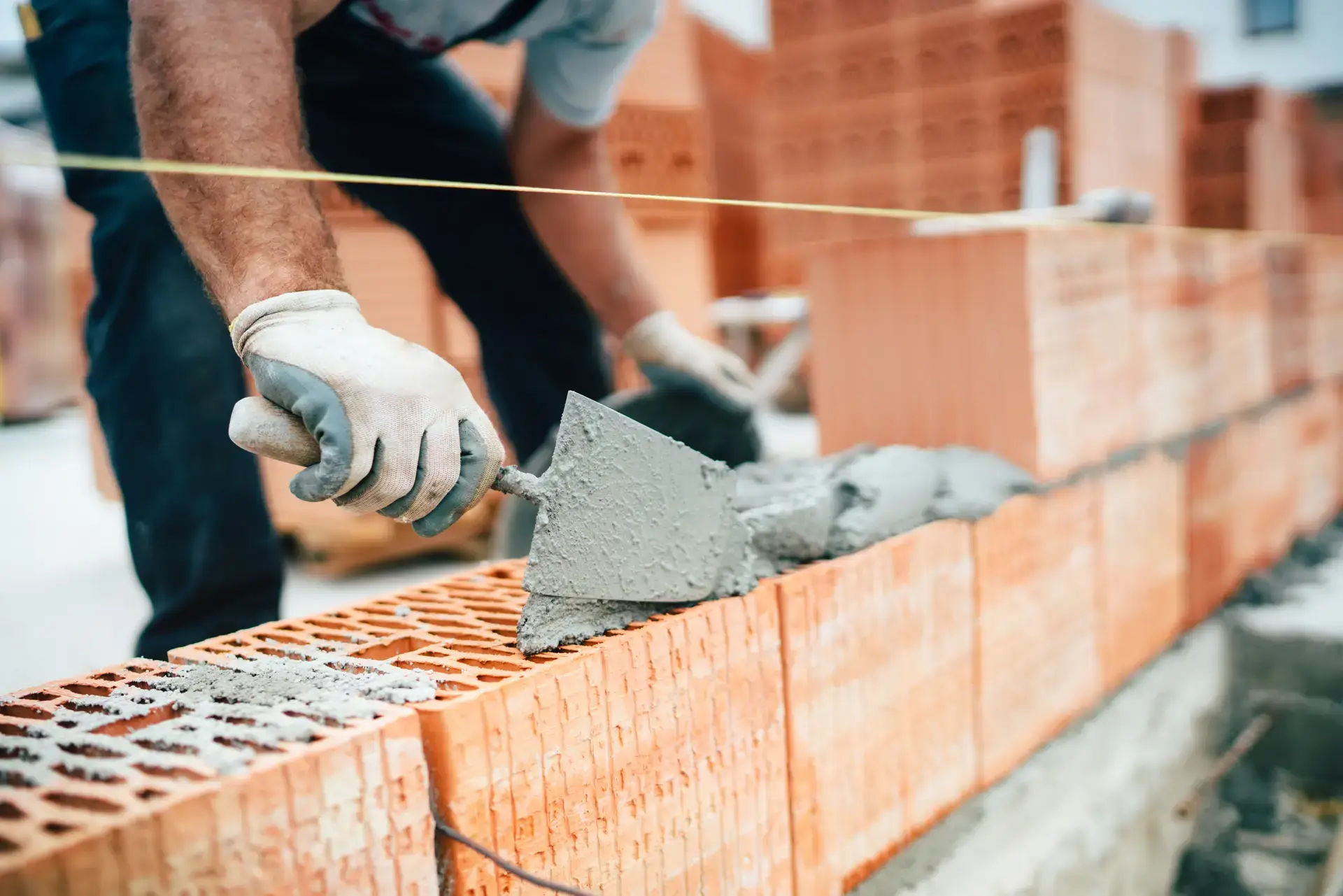 Close-up of a construction worker laying bricks and mortar for a wall, showcasing masonry skills and precision in alignment
