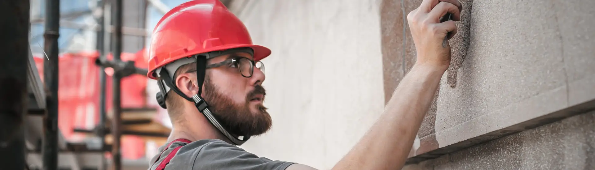 Construction worker in a red hard hat restores a concrete wall surface using a trowel, focusing on detailed repair work