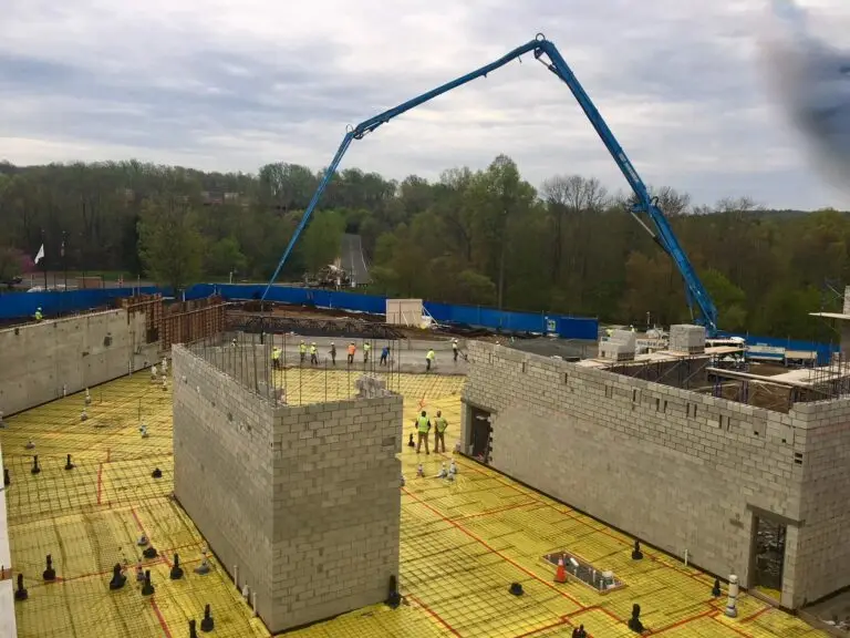 Masonry walls rise as crews prep for a major slab pour with rebar and vapor barriers in place. A concrete pump truck supports this large-scale foundation