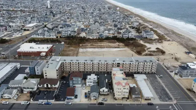 Overhead view of facade repair work on a coastal apartment building in Seaside Heights, NJ, with oceanfront dunes and dense housing nearby