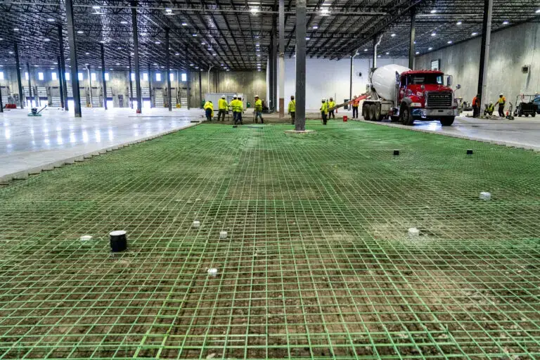 Crews prepare for a concrete slab pour in a warehouse tenant fit-out. Reinforced rebar is in place as a concrete truck begins the flooring process
